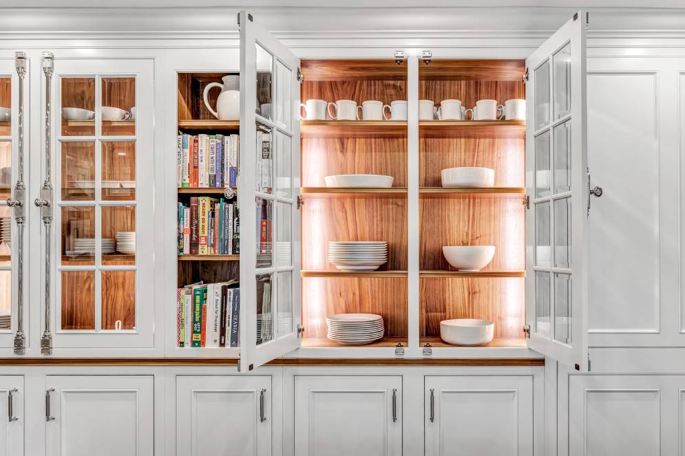 Wood-Mode walnut cabinet interiors with open glass doors, illuminated wood shelves and neatly arranged white dishes
